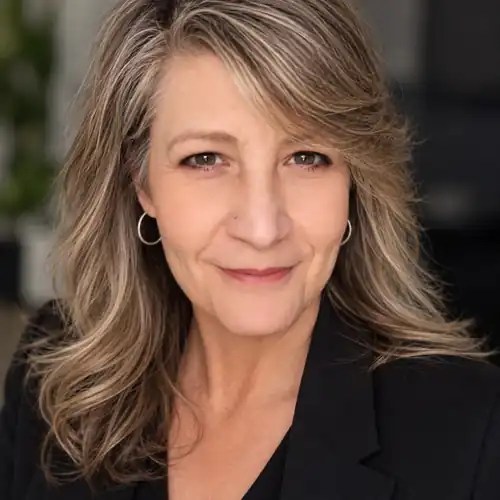 Lisa Proctor in a black blazer with long gray-blonde hair, facing the camera.